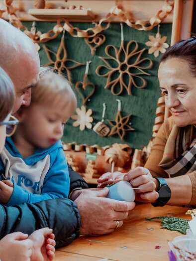 Eine Familie bastelt zusammen an einem Tisch. Zwei Kinder und ein Erwachsener arbeiten gemeinsam an einem Projekt.