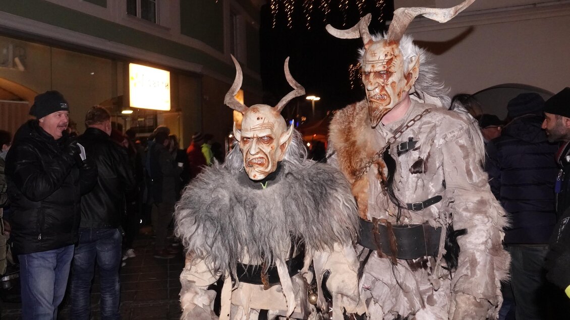 Zwei Menschen in fantasievollen Kostümen mit Hörnern und furchterregenden Masken stehen auf einer Straße. Im Hintergrund sind andere Zuschauer zu sehen, die das Geschehen beobachten. | © Tourismusverband Oststeiermark