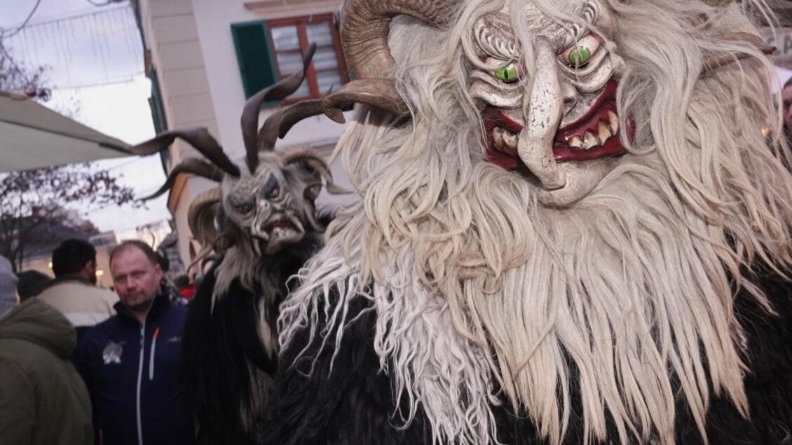 Eine festliche Parade mit traditionellen Kostümen, die gruselige Fratzen und Hörner zeigen. Menschen beobachten die Umgebung in einer lebhaften Atmosphäre. | © Tourismusverband Oststeiermark