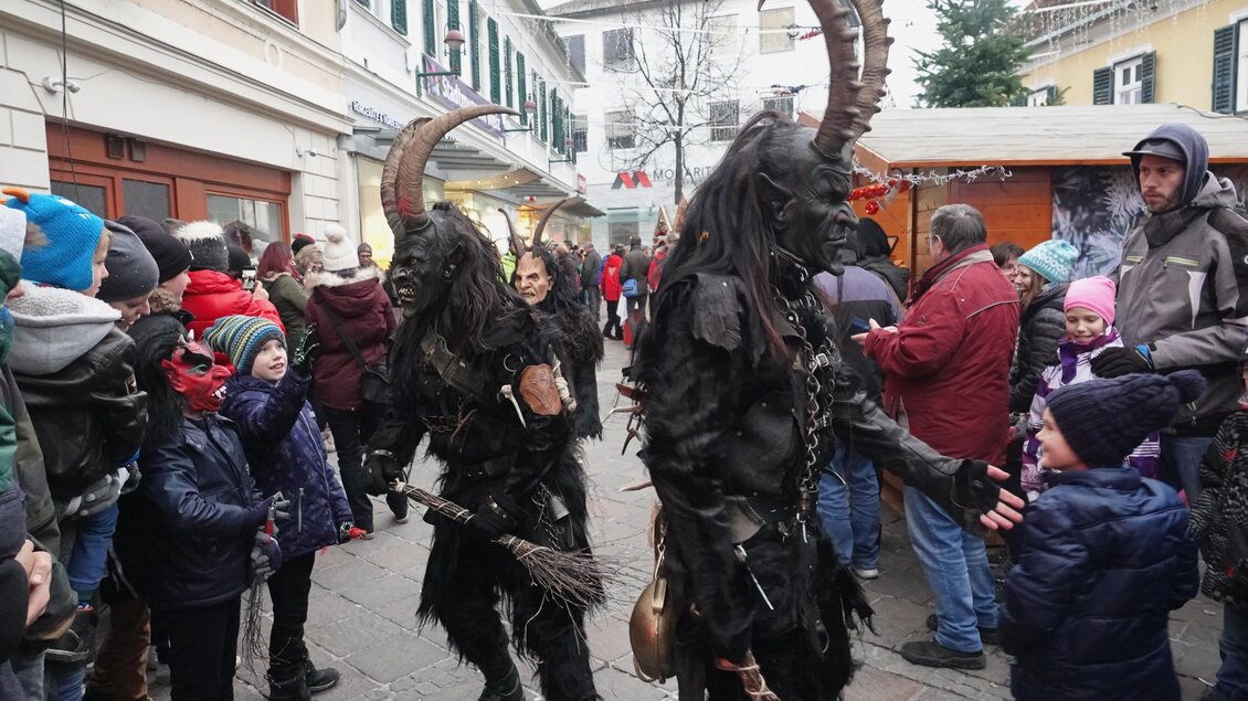 Zwei Krampus-Figuren in dämonischen Kostümen gehen durch eine Menschenmenge während eines Festes. Kinder und Erwachsene schauen neugierig zu. | © Tourismusverband Oststeiermark