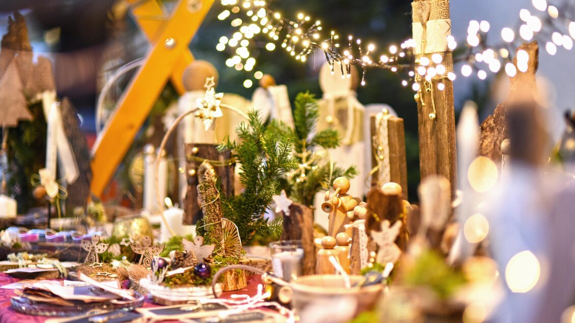 Ein festlich dekorierter Tisch mit handgemachten Kunstwerken und weihnachtlicher Beleuchtung. Die Atmosphäre ist warm und einladend, ideal für Weihnachtsmärkte. | © KK