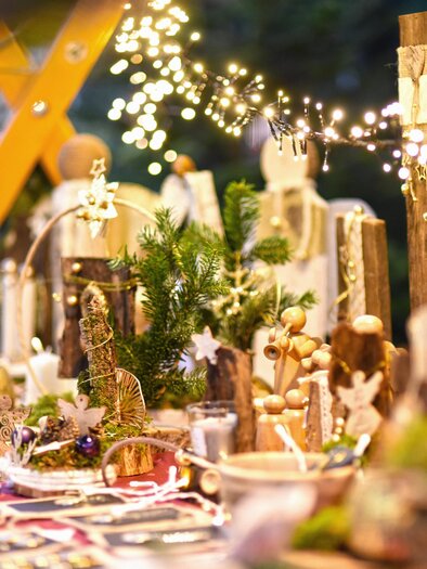 Ein festlich dekorierter Tisch mit handgemachten Kunstwerken und weihnachtlicher Beleuchtung. Die Atmosphäre ist warm und einladend, ideal für Weihnachtsmärkte. | © KK