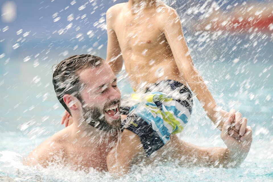 Ein Vater spielt fröhlich mit seinem Sohn im Wasser. Beide lachen und spritzen Wasser, während sie gemeinsam Spaß haben. | © H2O-Hoteltherme GmbH / Eisenberger