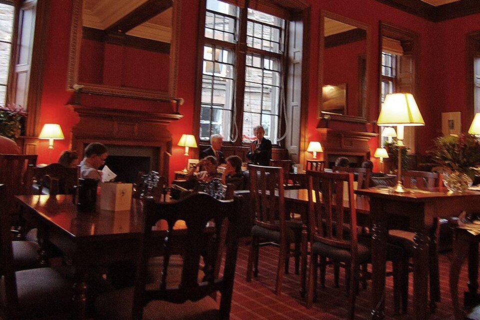 Ein gemütliches Café mit roten Wänden und großen Fenstern. Menschen sitzen an Tischen und genießen ihre Getränke in einer entspannten Atmosphäre.