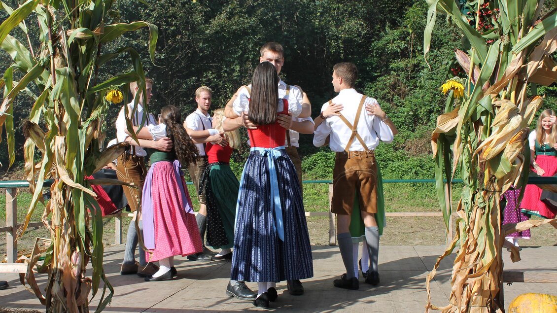 Eine Gruppe von Personen tanzt fröhlich in traditionellen Kleidern. Im Hintergrund sind Grünpflanzen und eine festliche Atmosphäre zu sehen. | © Marktgemeinde Wies