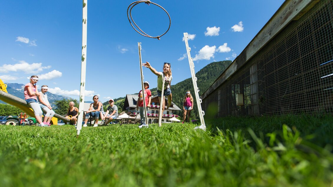 Eine Gruppe von Menschen spielt im Freien mit einem Reifenwurfspiel. Im Hintergrund sind Berge und ein blauer Himmel zu sehen. | © Dominik Steiner