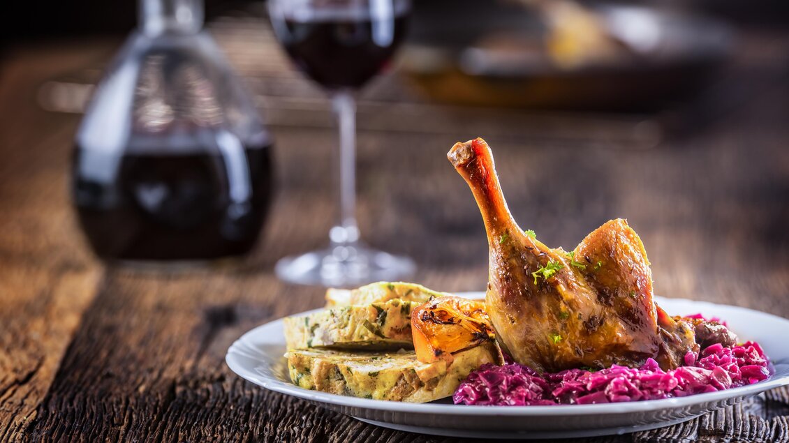 Ein köstliches Gericht mit gebratenem Hähnchenschenkel, Beilagen und roter Sauce. Im Hintergrund steht ein Glas Rotwein.