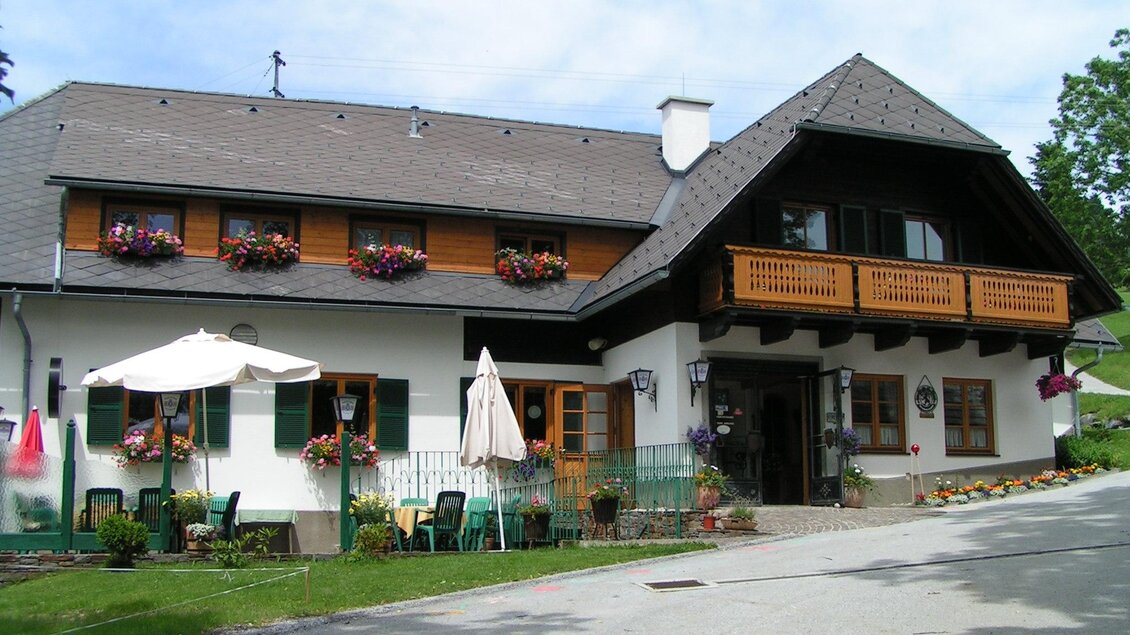 Ein charmantes Landhaus mit Holzverkleidung und blühenden Fenstern. Die Umgebung ist grün und einladend, ideal für eine entspannte Auszeit.