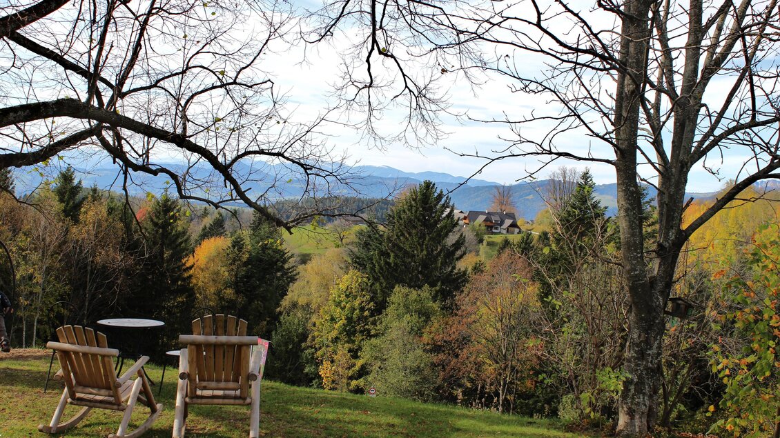 Ein schöner Ausblick auf grüne Wälder und Berge im Hintergrund. Zwei gemütliche Stühle stehen im Vordergrund.