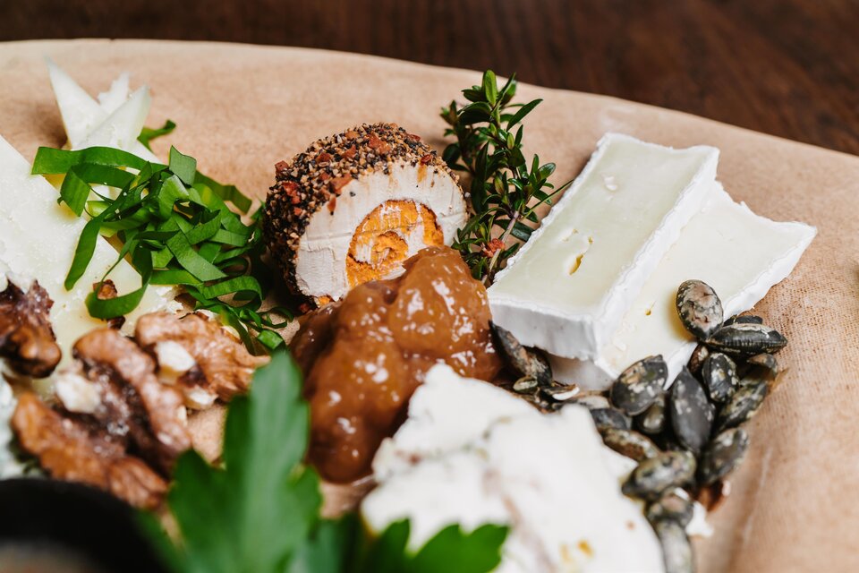 Ein Teller mit verschiedenen Delikatessen, darunter Käse, Nüsse und ein mit Gewürzen umhülltes Ei. Frische Kräuter und grüne Zwiebeln ergänzen das Bild. | © Michaela Lorber