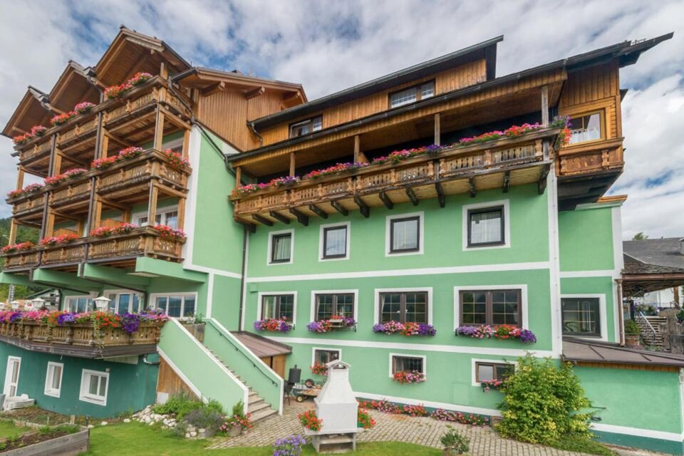 <p>Das Appartements-Restaurant Schwaiger, geschmückt mit Blumen auf den Balkonen. Die Fassade ist grün gestrichen und es gibt eine gemütliche Atmosphäre.</p> | © Hotel Schwaiger