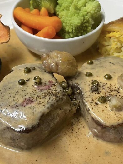 Ein köstliches Gericht mit zartem Fleisch in einer Sahnesauce, serviert mit buntem Gemüse und einer gefüllten Teigtasche. Auf dem Teller befinden sich außerdem eine Birne und eine kleine Schale mit Preiselbeermarmelade. | © Gasthof Steinmann