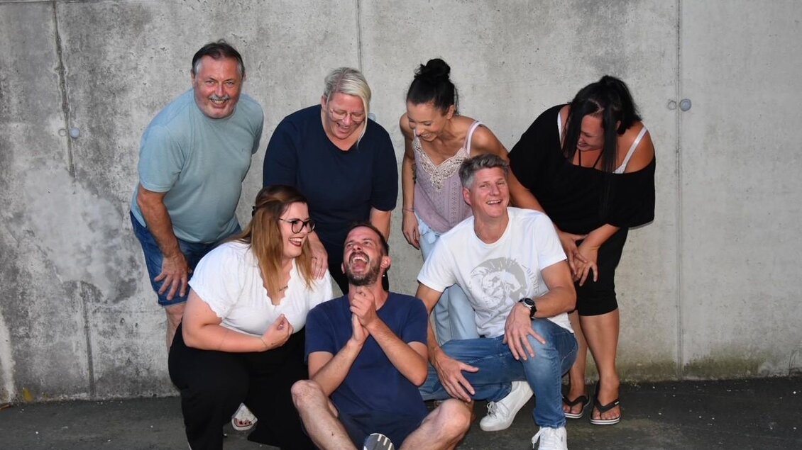 Eine Gruppe von glücklichen Menschen posiert vor einer grauen Wand. Sie lachen und haben Spaß miteinander. | © Theatergruppe Wildrose