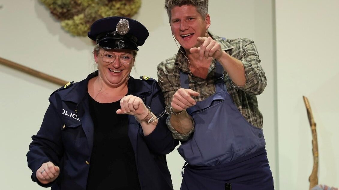 Ein fröhliches Duo auf der Bühne, ein Polizist und ein Mann in Arbeitskleidung. Sie scheinen eine witzige Unterhaltung zu führen und strahlen Spaß aus. | © Theatergruppe Wildrose