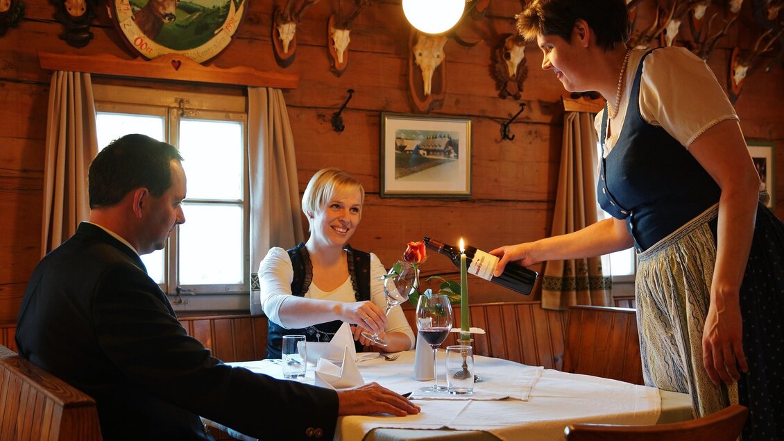 In einem gemütlichen Restaurant sitzt ein Paar am Tisch. Eine Kellnerin serviert eine Flasche Wein und eine Rose. | © Gasthof Unterberger