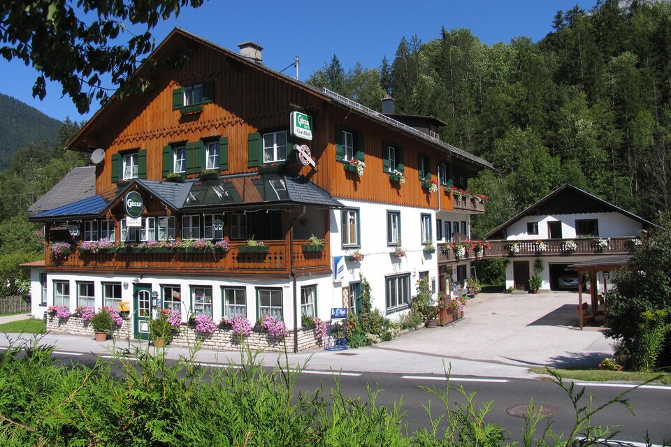 Ein charmantes Berghotel mit Holzfassade und blühenden Blumen. Umgeben von grünen Bäumen und klarem Himmel. | © Gasthof Staudnwirt