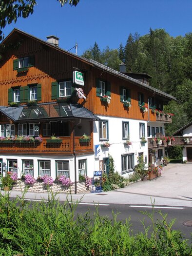 Ein charmantes Berghotel mit Holzfassade und blühenden Blumen. Umgeben von grünen Bäumen und klarem Himmel. | © Gasthof Staudnwirt