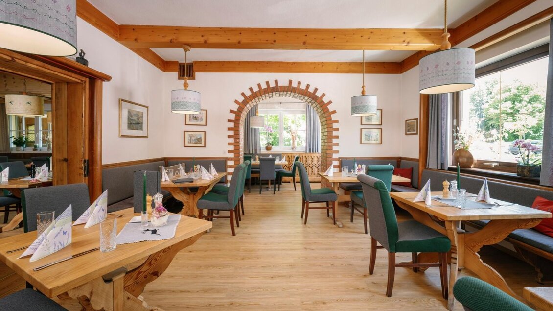 Ein einladendes Restaurant mit Holzmobiliar und gemütlicher Atmosphäre. Die Tische sind für Gäste gedeckt und große Fenster bieten Blick auf das Grün draußen. | © Dorfwirtshaus Stöckl