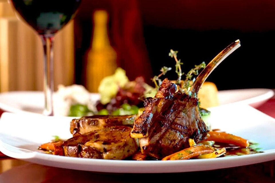 Ein köstliches Gericht mit gegrilltem Fleisch und buntem Gemüse auf einem weißen Teller. Im Hintergrund steht ein Glas Rotwein. | © GH Bachwirt