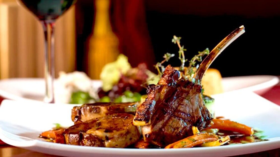 Ein köstliches Gericht mit gegrilltem Fleisch und buntem Gemüse auf einem weißen Teller. Im Hintergrund steht ein Glas Rotwein. | © GH Bachwirt