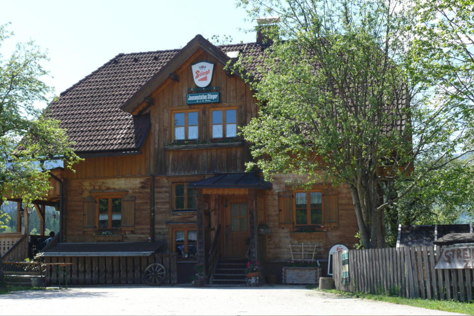 Ein traditionelles Holzhaus mit einem steilen Dach und zahlreichen Fenstern. Umgeben von Bäumen und einer einladenden Umgebung. | © Familie Pliem