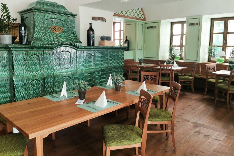 Das gemütliche Wirtshaus s`Johann mit Holztafeln und grünem Kachelofen. Die Fenster sind großzügig und bringen viel Tageslicht in den Raum. | © Wirtshaus s'Johann