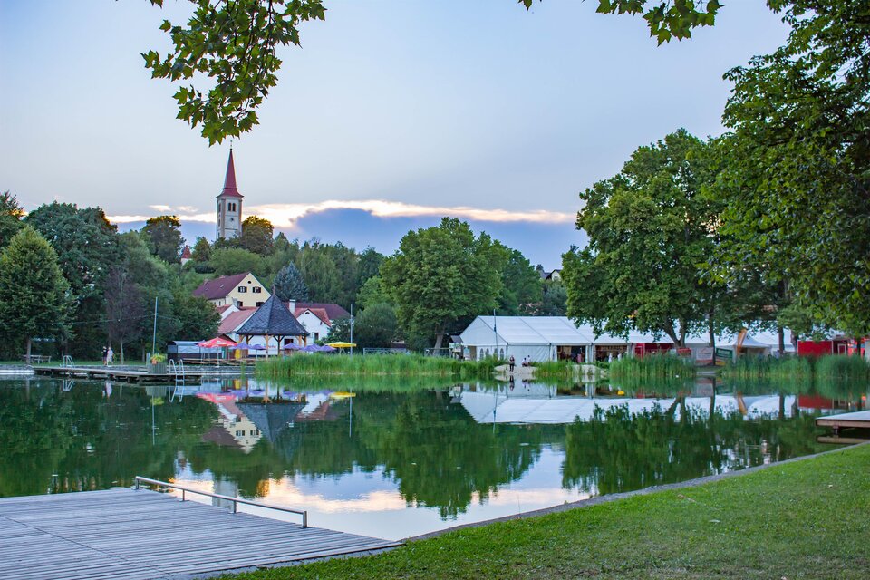 Ein schöner See umgeben von Bäumen und Gebäuden. Im Hintergrund ist der Kirchturm zu sehen. | © Sandra Brünner