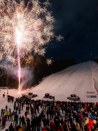 Ein beeindruckendes Feuerwerk leuchtet über einer verschneiten Piste. Viele Menschen stehen zusammen und genießen das festliche Spektakel. | © Michael Simonlehner