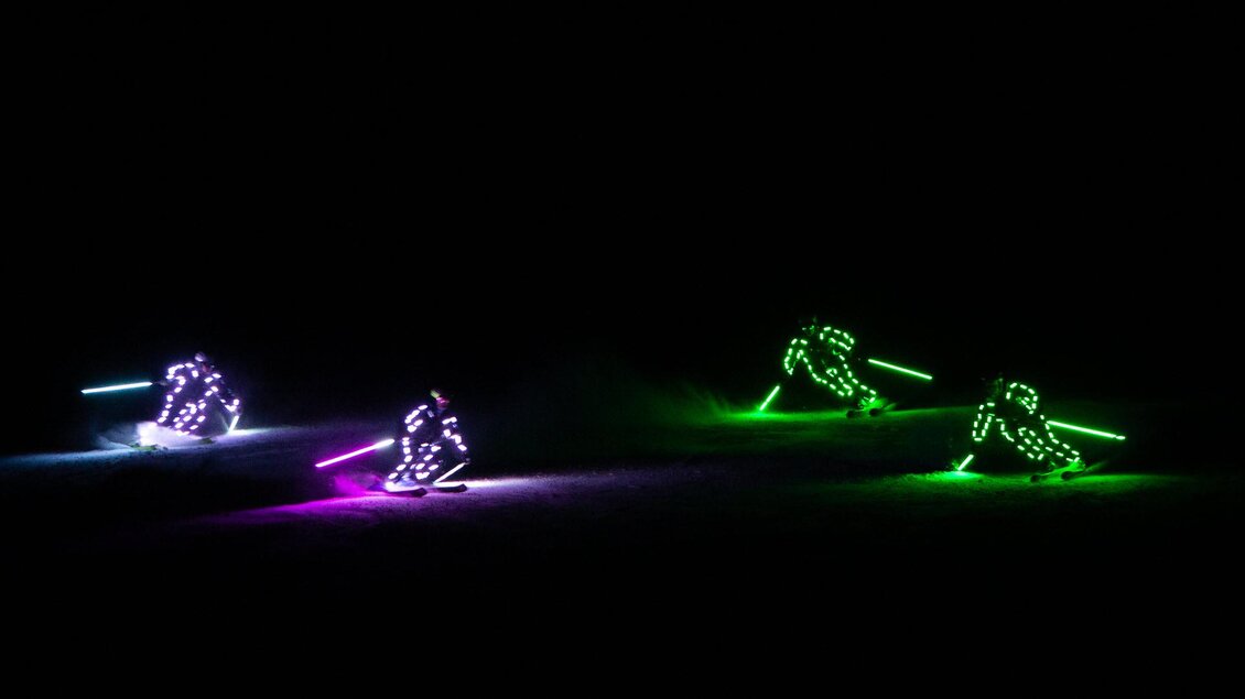 Vier Skifahrer mit leuchtenden Outfits fahren im Dunkeln. Die bunten Lichter erzeugen eine faszinierende Atmosphäre. | © Michael Simonlehner