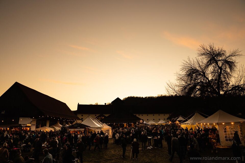 Ein lebhaftes Festival mit vielen Menschen, Ständen und festlicher Beleuchtung. Der Himmel färbt sich bei Sonnenuntergang in warmen Tönen. | © Roland Marx – copyright Grottenhof