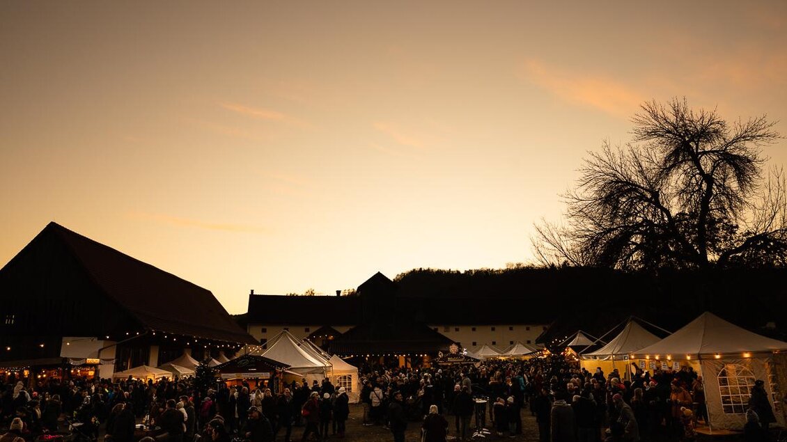 Ein lebhaftes Festival mit vielen Menschen, Ständen und festlicher Beleuchtung. Der Himmel färbt sich bei Sonnenuntergang in warmen Tönen. | © Roland Marx – copyright Grottenhof
