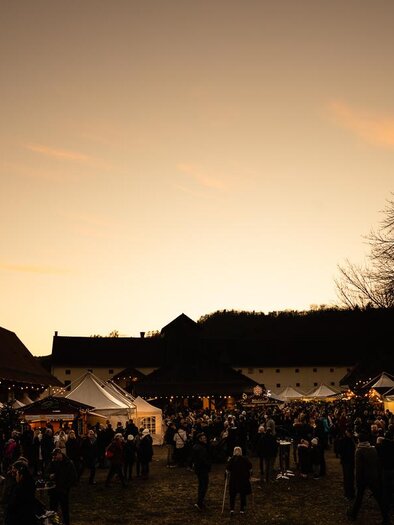 Ein lebhaftes Festival mit vielen Menschen, Ständen und festlicher Beleuchtung. Der Himmel färbt sich bei Sonnenuntergang in warmen Tönen. | © Roland Marx – copyright Grottenhof