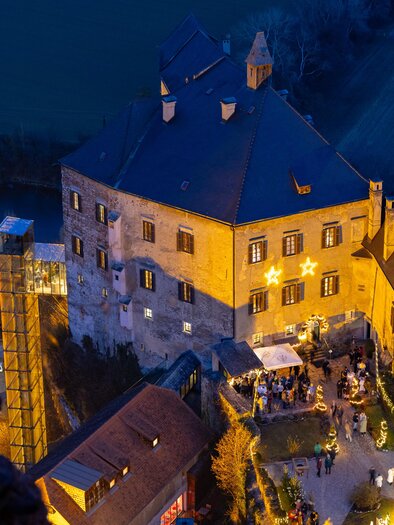 View from above of the illuminated Rabenstein Castle at dusk with Christmas lights, market stalls, and visitors. | © Region Graz-Harry Schiffer