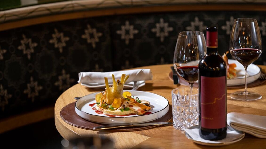 Ein elegant gedeckter Tisch mit einem kunstvoll angerichteten Gericht und Rotwein. Im Hintergrund sind Kristallgläser und eine geschmackvolle Atmosphäre zu sehen. | © Pierer Gastronomie GmbH