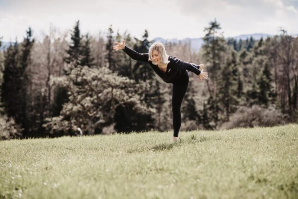 Eine Frau tanzt auf einer Wiese und balanciert im Freien. Im Hintergrund sind Bäume und ein bewölkter Himmel zu sehen. | © Erika Lange