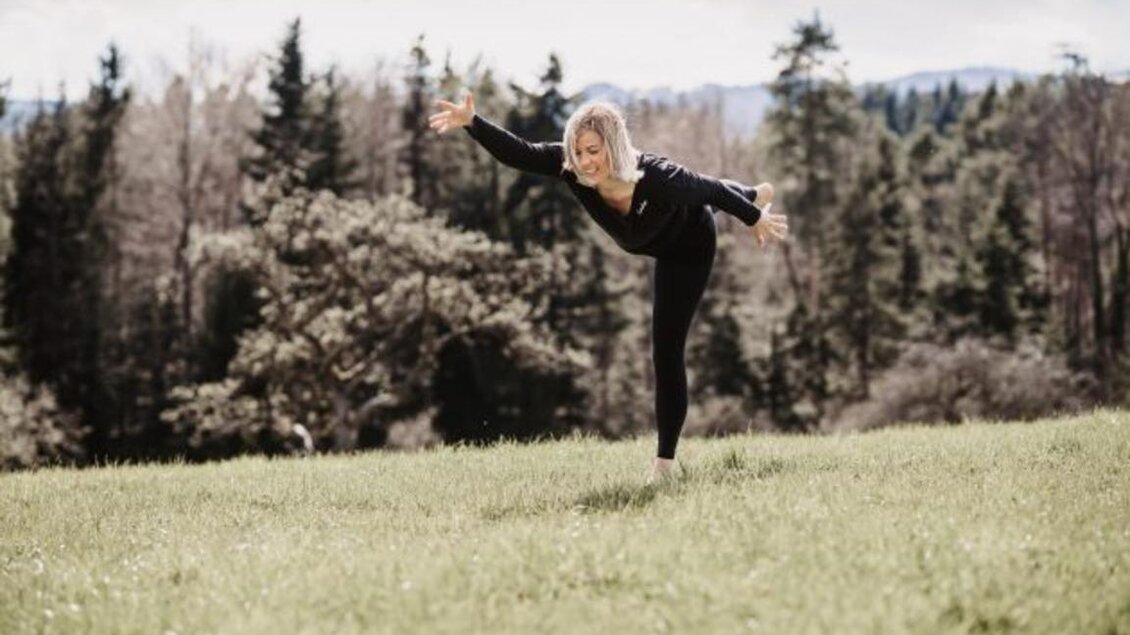 Eine Frau tanzt auf einer Wiese und balanciert im Freien. Im Hintergrund sind Bäume und ein bewölkter Himmel zu sehen. | © Erika Lange