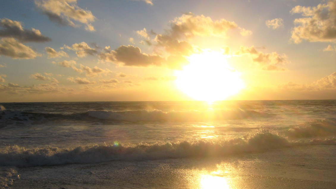 Ein wunderschöner Sonnenuntergang über dem Meer. Die Wellen brechen sanft am Strand und der Himmel ist mit Wolken gefüllt. | © Silvia Hinterholzner