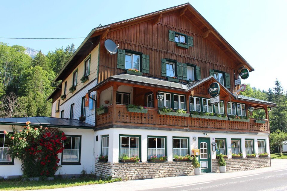 Ein traditionelles Gebäude im alpenländischen Stil mit einem schönen Holzvertäfelung. Umgeben von Bäumen und einer malerischen Landschaft. | © Gasthof Staud´nwirt, Bad Aussee, Außenansicht (c) TVB Ausseerland Salzkammergut_Lechner Viola