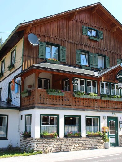 Ein traditionelles Gebäude im alpenländischen Stil mit einem schönen Holzvertäfelung. Umgeben von Bäumen und einer malerischen Landschaft. | © Gasthof Staud´nwirt, Bad Aussee, Außenansicht (c) TVB Ausseerland Salzkammergut_Lechner Viola