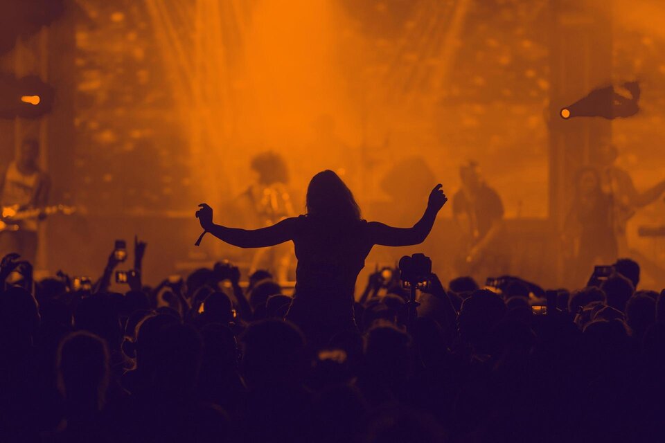 Eine lebhafte Konzertszene mit einer silhouette von einer Person, die zur Musik tanzt. Der Hintergrund ist in warmen Orangetönen gehalten und zeigt eine energiegeladene Atmosphäre. | © Pixabay