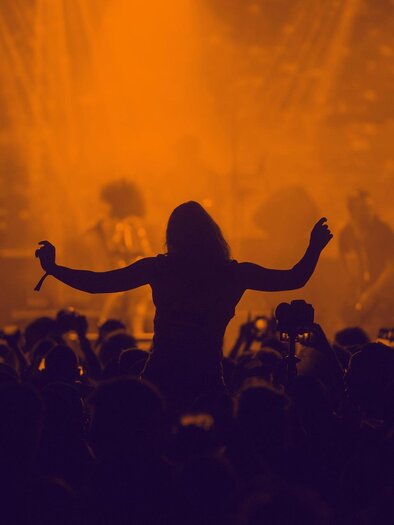 A lively concert scene with a silhouette of a person dancing to the music. The background is in warm shades of orange and displays an energetic atmosphere. | © Pixabay