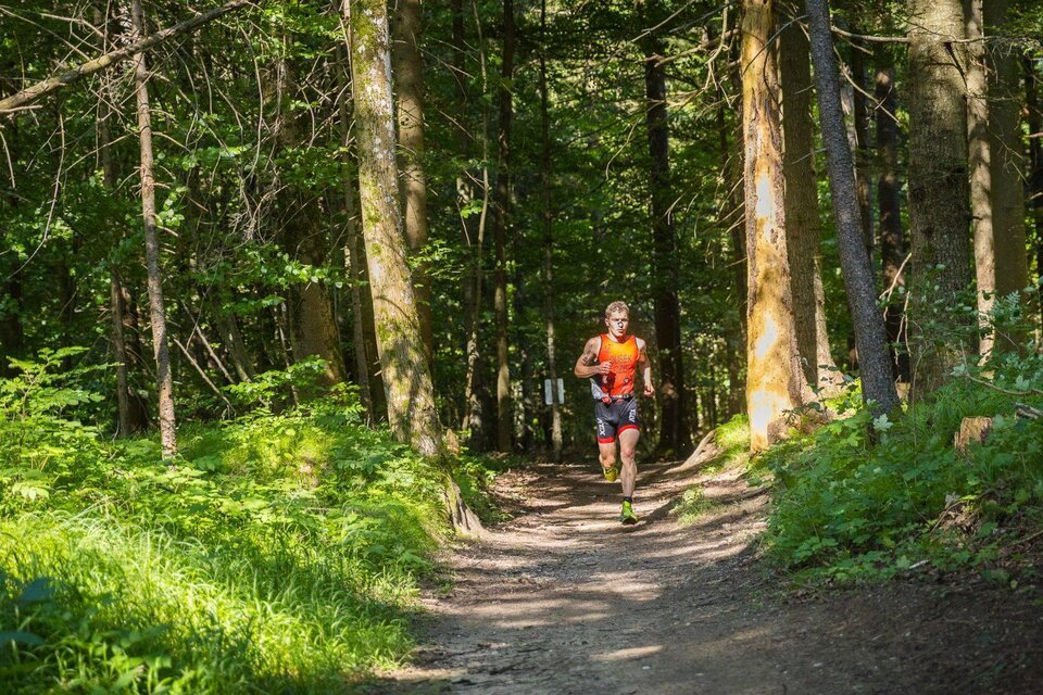 <p>Ein sportlicher Läufer vom Xterra Austria Triathlon läuft auf einem schmalen Weg durch einen grünen Wald in Altaussee. Die Sonne scheint durch die Bäume und beleuchtet die Landschaft.</p> | © XTERRA Austria
