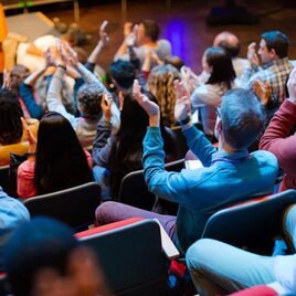 Ein Publikum applaudiert in einem Veranstaltungsraum. Die Zuschauer sitzen in Reihen und zeigen Begeisterung für die Präsentation. | © AdobeStock_455882231