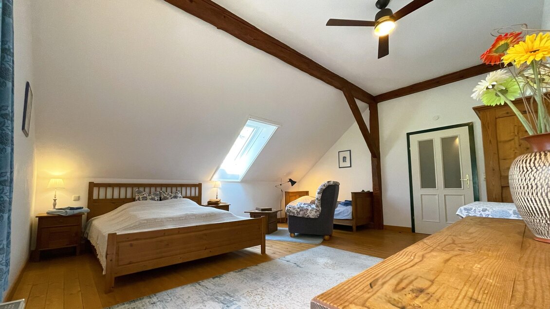 Ein gemütliches Schlafzimmer mit einem Holzbett und einem Sessel. Der Raum hat Dachschrägen und ist hell und freundlich eingerichtet. | © Paul Strasser