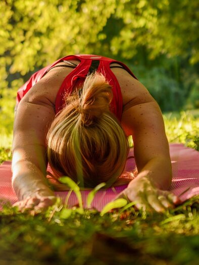 Eine Person macht Yoga in einer entspannten Position auf einer Matte im Freien. Die Umgebung ist grün und sonnig. | © Pixabay