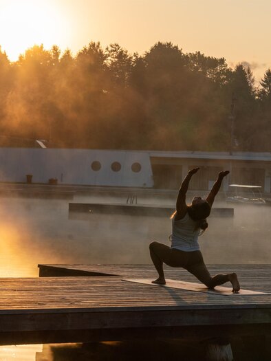 A woman practicing yoga at sunrise on a wooden platform at the natural bathing pond Weihermühle. | © Fuchs Sandra