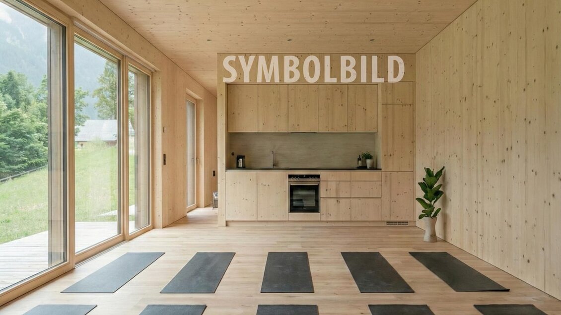 Ein heller Yoga-Raum mit Holzverkleidung und großen Fenstern. Auf dem Boden liegen mehrere Yogamatten in einer ordentlichen Anordnung.