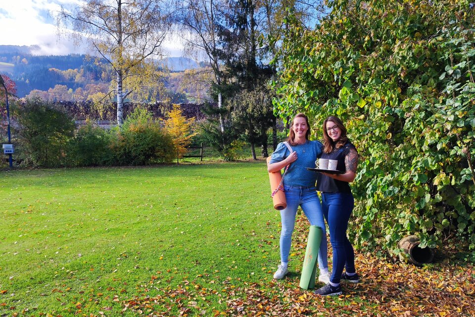 Zwei Frauen stehen auf einer grünen Wiese und lächeln. Im Hintergrund sind Bäume und eine schöne Landschaft zu sehen. | © Marlies Eichelberger