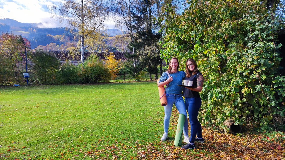 Zwei Frauen stehen auf einer grünen Wiese und lächeln. Im Hintergrund sind Bäume und eine schöne Landschaft zu sehen. | © Marlies Eichelberger