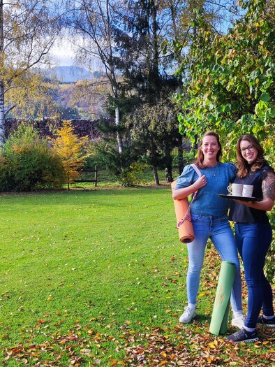 Zwei Frauen stehen auf einer grünen Wiese und lächeln. Im Hintergrund sind Bäume und eine schöne Landschaft zu sehen. | © Marlies Eichelberger